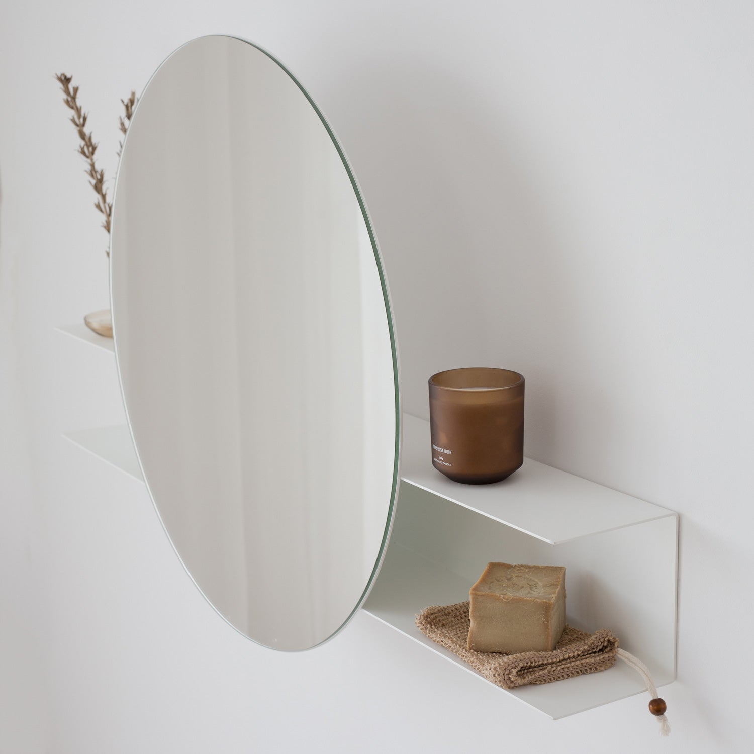 white round mirror on a white wall with a candle and soap on a small shelf.