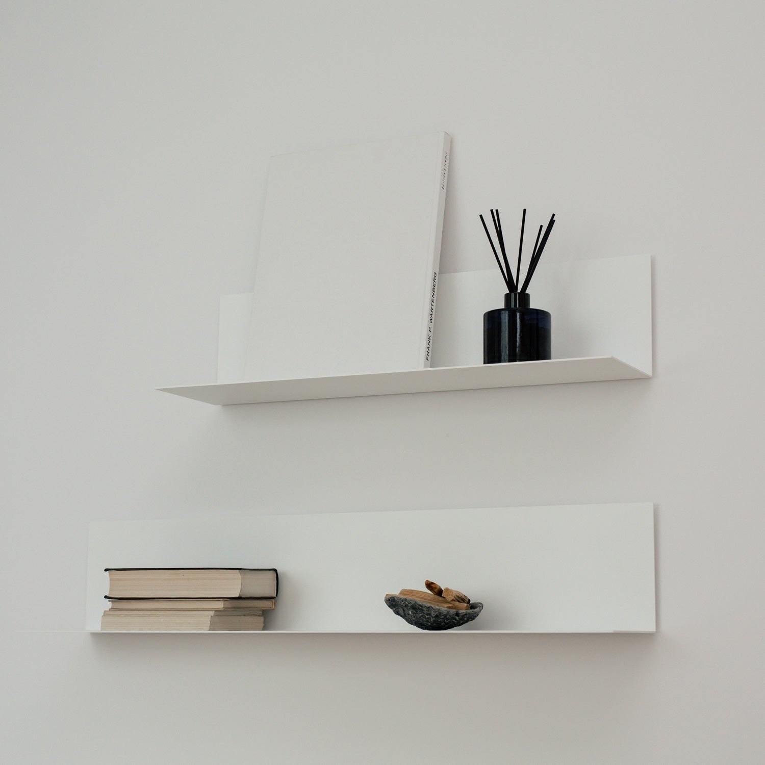 Two modern white shelves on white wall with black decorations and books